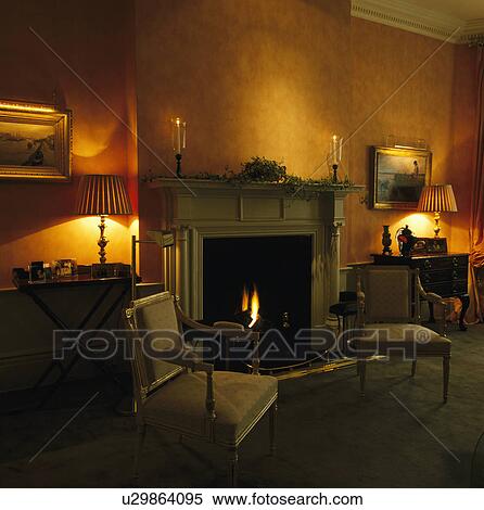 Lighted lamps on either side of fireplace in traditonal living room View Large Photo Image Stock Photography - Lighted lamps on either side of fireplace in traditonal living room. Fotosearch