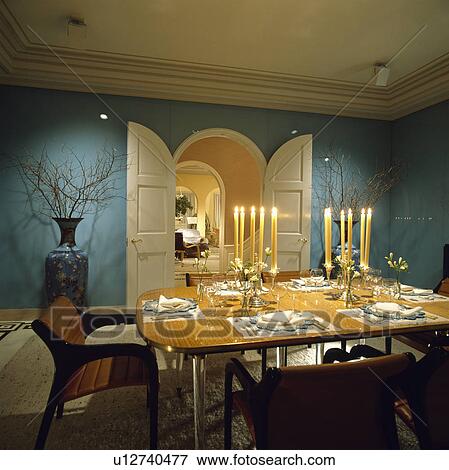 Stock Photo - Lighted yellow candles and place settings on eighties table in turquoise dining room with open double white doors. Fotosearch