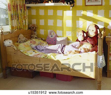 Little Girl Laying On Pine Bed With Stuffed Toys In Yellow And White Painted Bedroom Stock Image