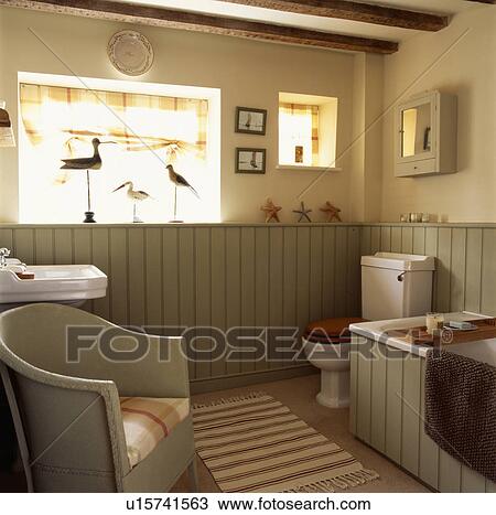 Stock Image - Lloyd Loom chair in cream Shaker-style cottage bathroom with pale green panelling to dado height. Fotosearch
