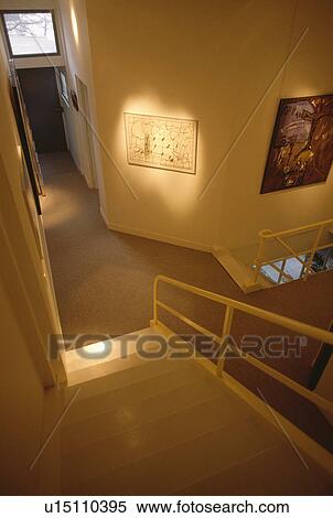 Stock Photography - Looking down modern stairs with metal bannisters to small hall with beige carpet. Fotosearch