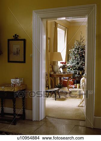 Picture - Looking into livingroom which is decorated with large Christmas tree from yellow painted hallway.. Fotosearch