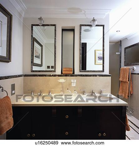 Stock Photo - Marble framed mirrors above circular basins unset in travertine topped vanity unit in modern white bathroom . Fotosearch