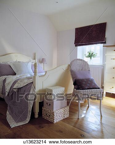 Picture - Mauve throw on cream wooden bed in mauve attic bedroom with wooden flooring and purple blind and white cane chair. Fotosearch