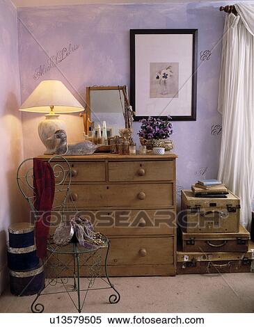 Metal chair and antique pine chest of drawers with lighted lamp in mauve cottage bedroom with old leather suitcases View Large Photo Image Stock Photography - Metal chair and antique pine chest of drawers with lighted lamp in mauve cottage bedroom with old leather suitcases. Fotosearch