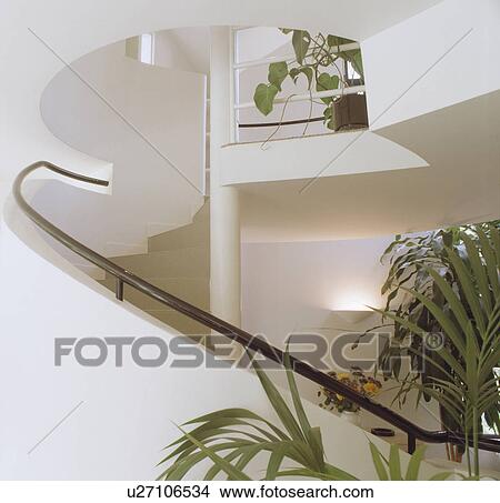 Picture - Metal handrail on curved wall of modern staircase in white hall with green houseplants . Fotosearch
