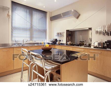 Metal stools at breakfast bar on island unit with black granite worktop in modern kitchen with pale wood fitted cupboards View Large Photo Image Stock Image - Metal stools at breakfast bar on island unit with black granite worktop in modern kitchen with pale wood fitted cupboards. Fotosearch