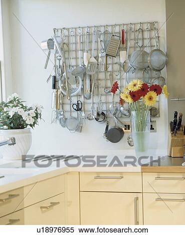 Stock Photography - Metal utensils and sieves on stainless steel grid storage rack in modern kitchen with flowers in vase on worktop. Fotosearch
