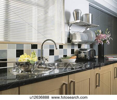 Stock Photo - Metallic blind above double circular stainless steel sinks in modern kitchen with steel shelving above granite worktop. Fotosearch