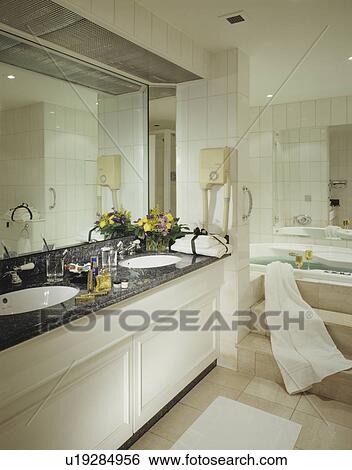 Stock Photograph - Mirror above basins underset in granite-topped vanity unit in modern bathroom. Fotosearch