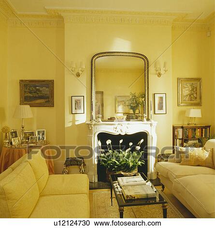 Stock Image - Mirror above fireplace in yellow traditional living room with yellow sofas. Fotosearch