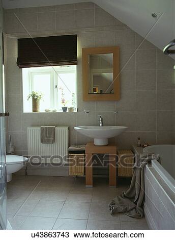 Stock Image - Mirror above modern white basin on wooden base in modern limestone tiled bathroom. Fotosearch