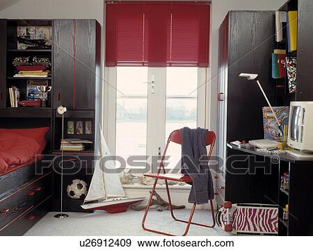 Stock Photo - Model sailing boat and red metal chair in front of French windows with red blind in child's bedroom with black units. Fotosearch