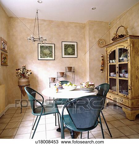 Stock Image - Modern blue metal chairs in dining room with marbled paint effect walls and cream tiled floor. Fotosearch