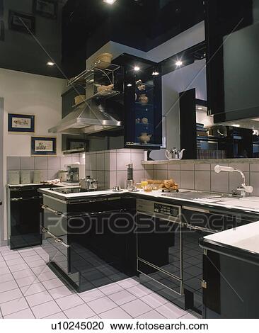 Stock Image - Modern kitchen with black fitted cupboards and white tiled floor. Fotosearch
