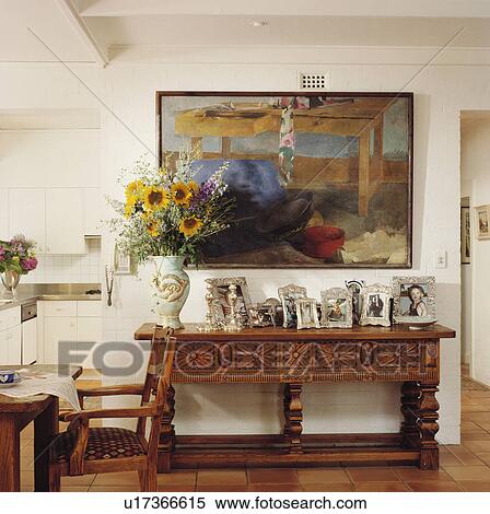 Stock Photography - Modern picture above carved wood console table with black+white photographs in openplan white hall. Fotosearch
