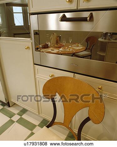 Modern wooden chair in front of steel oven with kitchen reflected in glass panel View Large Photo Image Stock Photo - Modern wooden chair in front of steel oven with kitchen reflected in glass panel. Fotosearch
