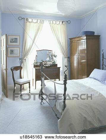 Modern Wrought Iron Bed In Pastel Blue Bedroom With White Curtains And Carpet And Antique Wardrobe Stock Image