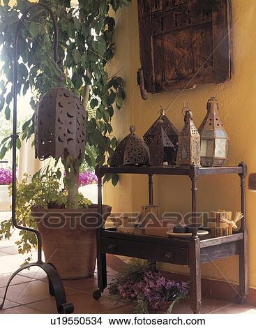 Picture - Moroccan metal lanterns on wooden trolley beside tall houseplant in terracotta pot. Fotosearch