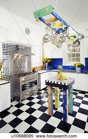 Stock Photography - Multicoloured rack above matching table in modern white kitchen with black range oven and black+white flooring. Fotosearch