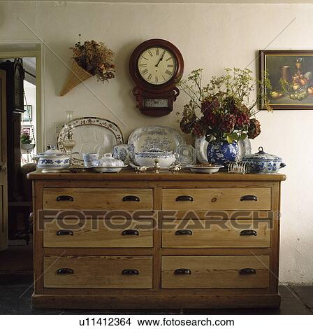 Picture - Old blue and white plates and tureens on pine chest of drawers below antique clock. Fotosearch
