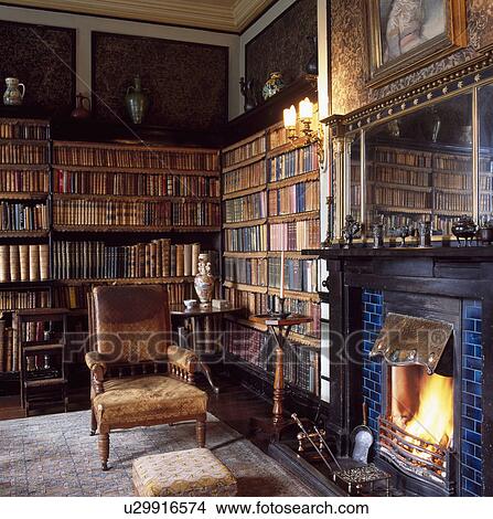 Old Edwardian leather armchair beside fireplace with lighted fire in country study library with leatherbound books on the shelves View Large Photo Image Picture - Old Edwardian leather armchair beside fireplace with lighted fire in country study library with leatherbound books on the shelves. Fotosearch