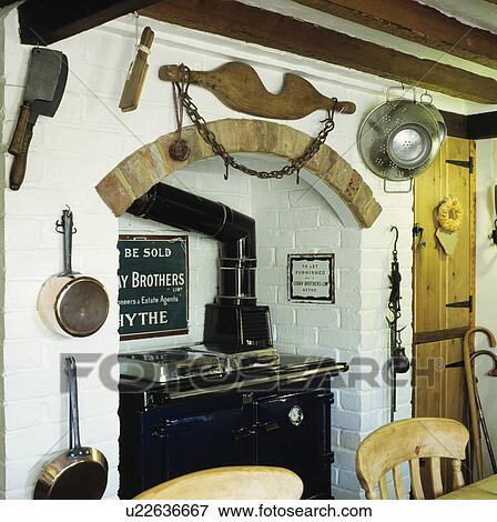 Stock Photo - Old kitchen utensils and milkmaids yoke above recessed black stove in white country kitchen. Fotosearch