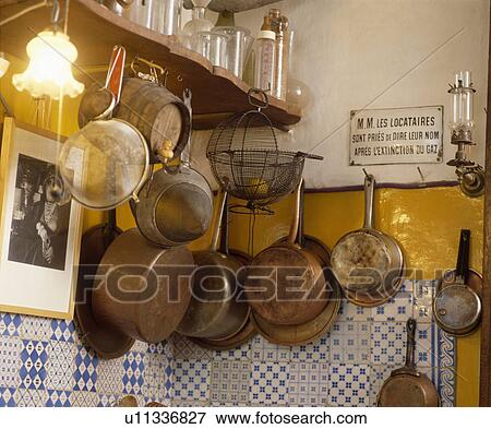 Stock Photo - Old metal sieves and copper saucepans on wall above blue+white tiles in French kitchen. Fotosearch