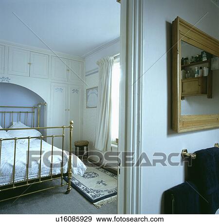 Open bathroom doorway with view of brass bed in alcove below fitted cupboards in traditional white bedroom View Large Photo Image Stock Photo - Open bathroom doorway with view of brass bed in alcove below fitted cupboards in traditional white bedroom . Fotosearch