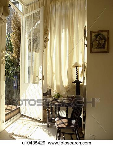 Stock Photo - Open half-glazed door and white curtain in small cream hall with wooden table and chair. Fotosearch