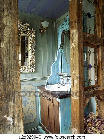 Stock Image - Open rustic wooden door to small green panelled bathroom with basin fitted into turquoise cupboard. Fotosearch