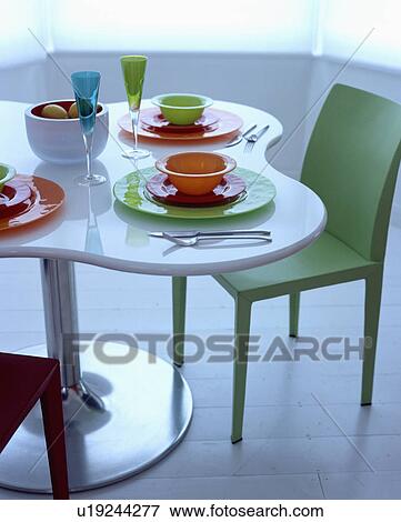 Stock Photo - Orange and green bowls and plates on white table with metal pedestal beside green Jasper Morris 'Air' chair. Fotosearch