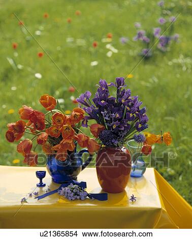 Picture - Orange tulips and blue irises in orange and blue jugs on yellow tablecloth. Fotosearch