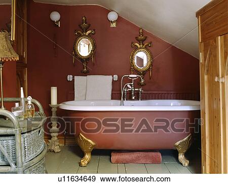 Stock Photo - Ornate antique gilt mirrors above clawfoot bath in small terracotta attic bathroom. Fotosearch