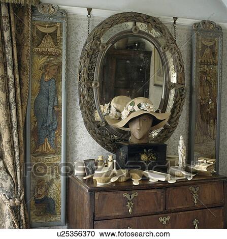 Stock Image - Painted pictorial panels on either side of carved antique mirror above collection of old ivory brushes on chest of drawers . Fotosearch