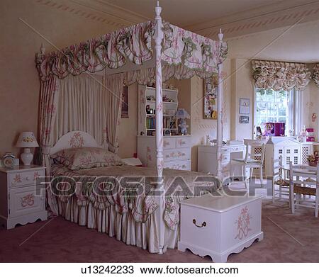 Stock Image - Painted white wooden chest with pink motif below bed with pink+green drapes and bedcover in child's bedroom. Fotosearch
