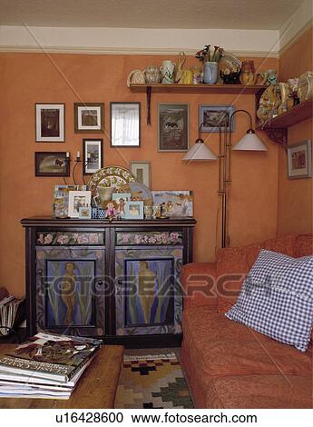 Stock Image - Painted wooden cupboard and orange sofa in terracotta living room. Fotosearch