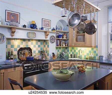 Stock Photography - Pans on storage rack above island unit in traditional kitchen with black range oven and green and yellow wall tiles. Fotosearch