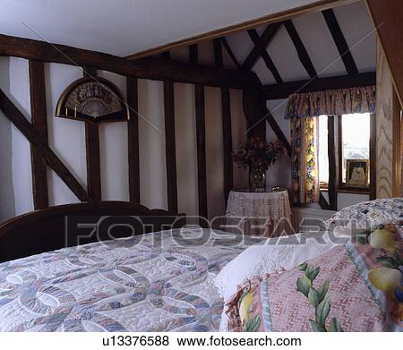 Stock Photo - Pastel patchwork quilt on bed in small cottage bedroom with exposed wall beams. Fotosearch