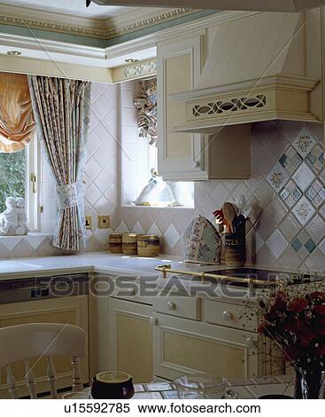Stock Photography - Pastel wall tiles above hob built into kitchen unit with brass safety rail. Fotosearch