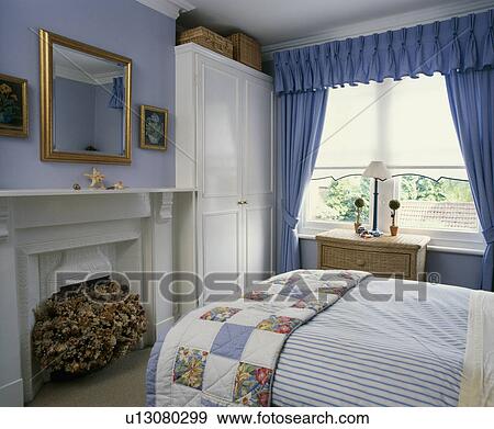 Patchwork Quilt On Bed In Pale Blue Bedroom With White Built In Cupboard And Blue Curtains Stock Photo