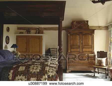 Patchwork quilt on four-poster bed in country bedroom with antique oak linen press View Large Photo Image Stock Photo - Patchwork quilt on four-poster bed in country bedroom with antique oak linen press. Fotosearch