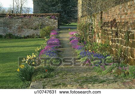 Stock Image - Path beside tone wall in country garden in Spring. Fotosearch