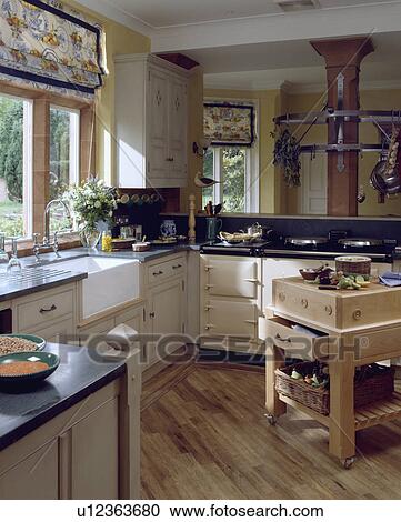 Patterned blind above white ceramic sink in cottage kitchen with cream aga and wooden flooring View Large Photo Image Stock Image - Patterned blind above white ceramic sink in cottage kitchen with cream aga and wooden flooring. Fotosearch