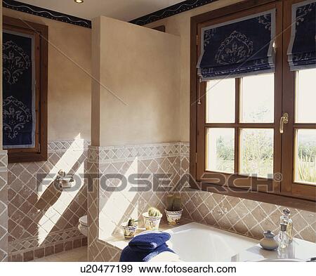 Stock Photo - Patterned blue blinds on window above bath in Miediterranean bathroom with beige tiles. Fotosearch