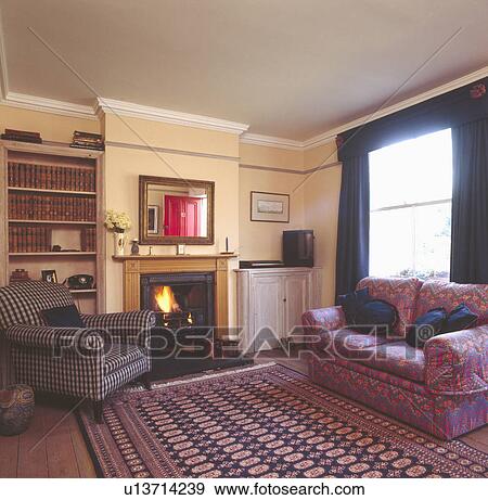 Stock Photo - Patterned oriental rug on wooden flooring in living room with checked armchair and patterned sofa. Fotosearch