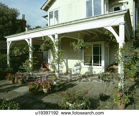 Stock Image - Paved patio in front of traditional white country house with veranda. Fotosearch