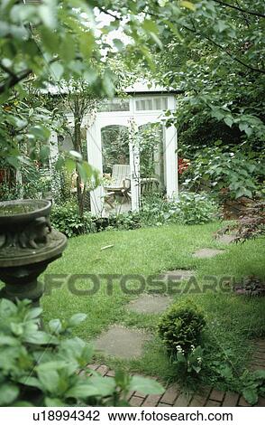 Stock Image - Paving path across lawn to traditional conservatory extension in country garden. Fotosearch