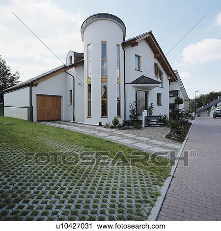 Stock Image - Paving setts in grass at the side of modern white house in country village. Fotosearch