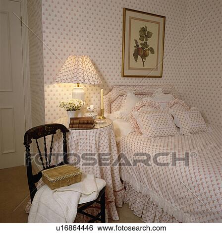 Peach spotted wallpaper and matching lamp and bedlinen in small bedroom with wicker box on antique chair View Large Photo Image Stock Photograph - Peach spotted wallpaper and matching lamp and bedlinen in small bedroom with wicker box on antique chair. Fotosearch